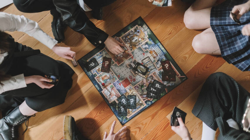 Människor sitter på golvet runt ett bordspel och spelar.
