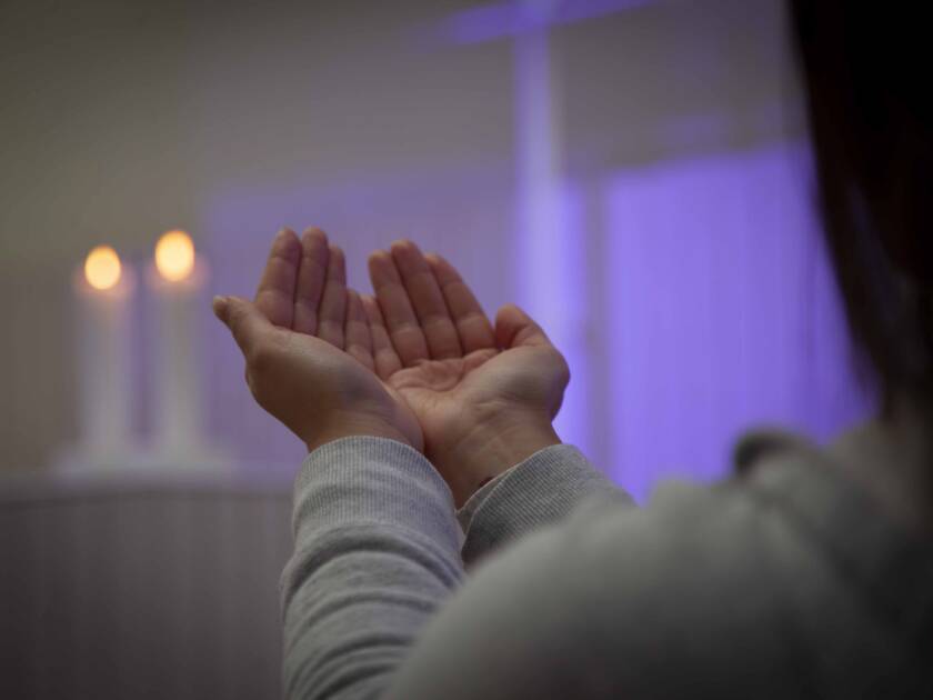 Hämärässä tilassa nainen nostanut kätensä eteensä kämmenet ylöspäin, taustalla kaksi kynttilää