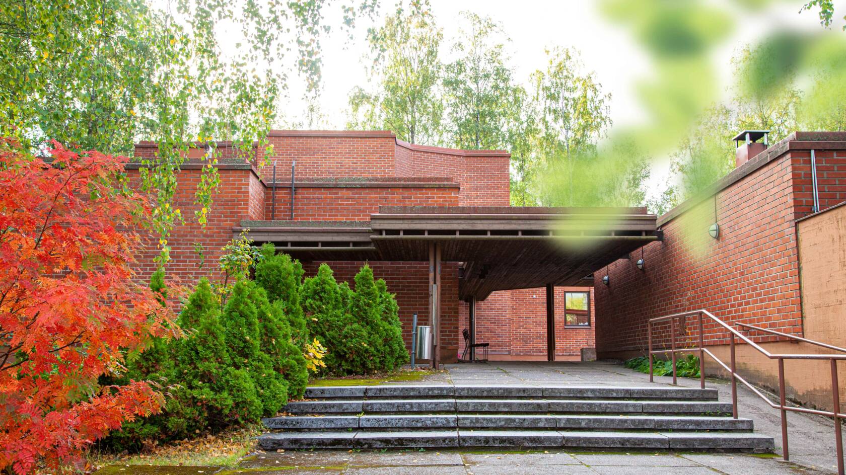 Kivistön kirkolle vievät leveät ja matalat portaat, joiden ympärillä puita ja pensaita syksyn väreissä