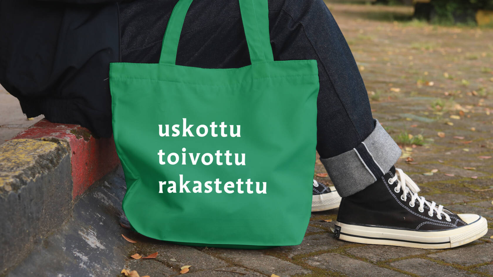 Maahan on laskettu kangaskassi, jossa lukee uskottu toivottu rakastettu. Ihminen istuu portailla kassin kanssa.