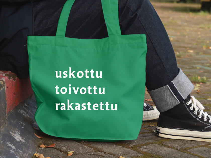 Maahan on laskettu kangaskassi, jossa lukee uskottu toivottu rakastettu. Ihminen istuu portailla kassin kanssa.