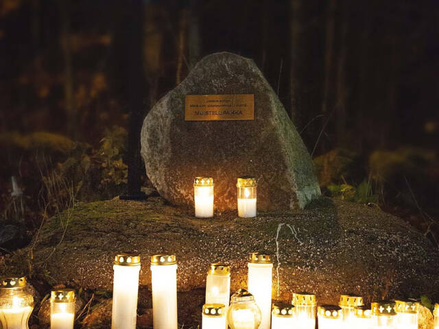Seutulan kappelin muistelupaikka. Kivi jossa muistolaatta. Kiven edessä palaa kynttilöitä. On pimeää.