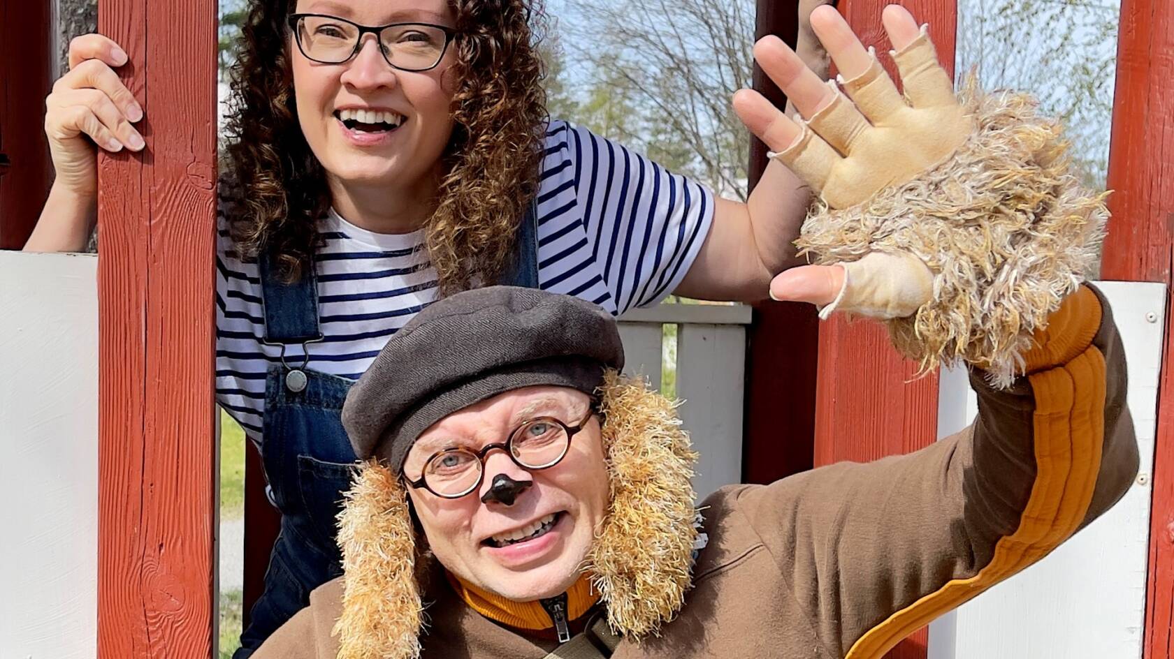 Koiraksi pukeutunut ihminen ja nainen vilkuttavat sekä hymyilevät kameralle.
