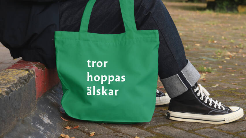 Person som sitter med tygkasse med texten "tror hoppas älskar".