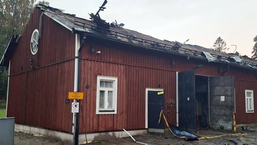 Palanut punainen rakennus, osittain katto poikki, taustalla puita ja pilvet.